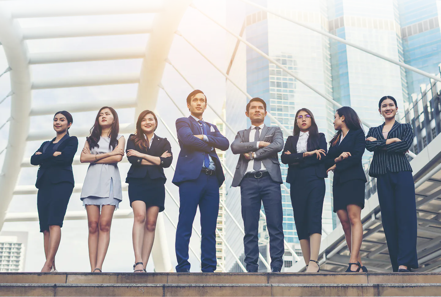 A group of diverse professional business people in suits standing in front of modern architectural bridge and skyscrapers